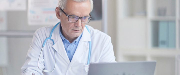 Médico de meia-idade com estetoscópio azul olhando o computador.