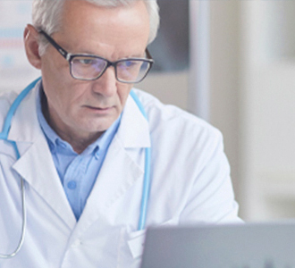 Médico de meia-idade com estetoscópio azul olhando o computador.