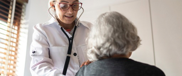 Médica examinando paciente idosa com estetoscópio.