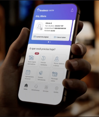 Mão segurando celular com o aplicativo Bradesco Saúde aberto na tela inicial.